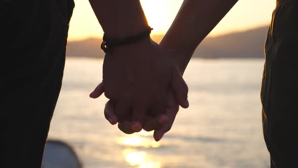 Silhouette of Male and Female Hands Holding Each Other at Sunset Against an Sea Background. Young