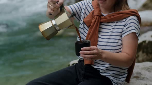 Woman hands pours coffee  from Mocha Pot against mountain river