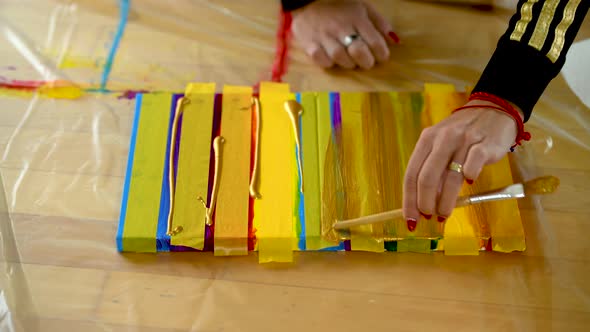 A woman using painters tape to finish her colorful stripes on a canvas