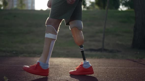 Side View Prosthetic Legs of Male Amputee Walking in Sunrays in Slow Motion on Red Sports Track