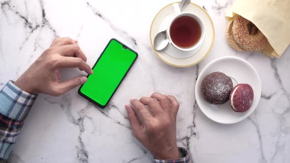 Top View of Man Hand Using Smart Phone with Tea and Cookies on Table