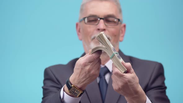 Senior Adult man in glasses and an office suit with a tie recounts dollar bills close-up