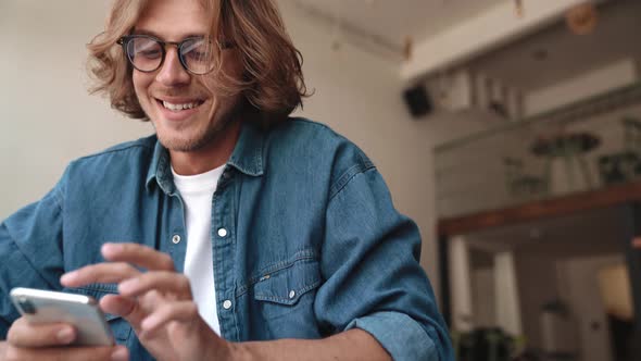 Happy blond man in eyeglasses texting on mobile