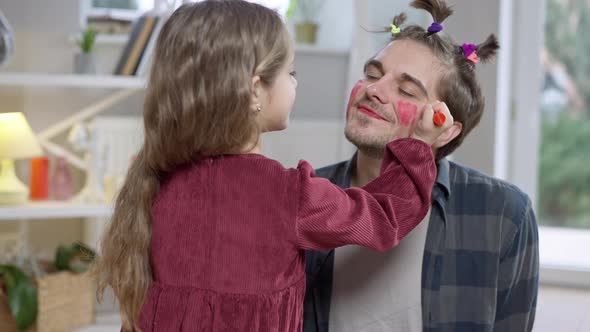 Funny Man with Ponytails Smiling As Girl Painting His Cheeks with Red Marker