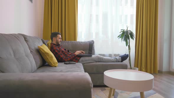 Man in Classic Square Shirt Lying on a Couch and Video Conference on Laptop PC at Home