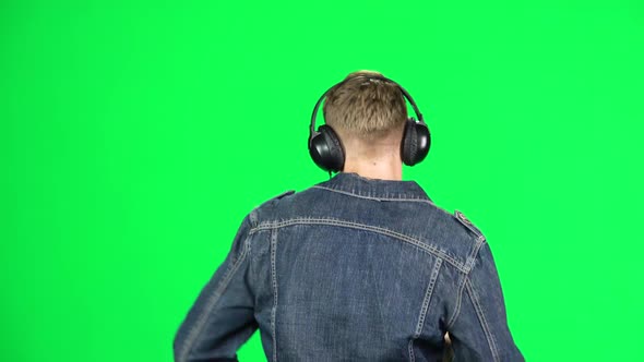 Man in Big Headphones Goes, Listening Music and Dancing with Smartphone on Green Screen at Studio