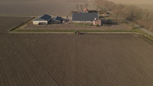 Countryside farm building, tractor plowing the field, Birds flying around, Aerial static view