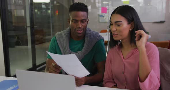 Diverse male and female business colleagues sitting at desk analyzing document and smiling