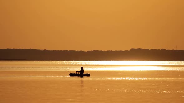 Fisherman in a boat at golden sunset time. Silhouette of man floating with oars