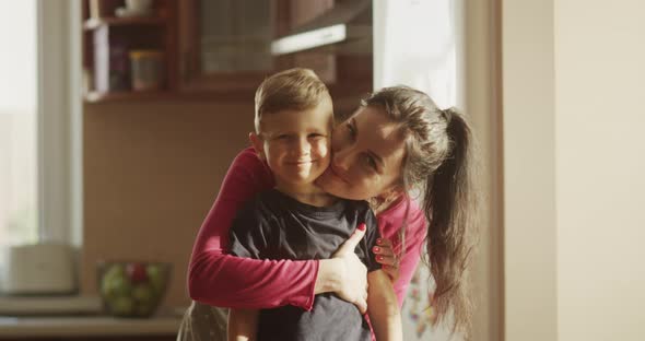 Portrait Of Mother And Child Boy Smiling And Looking At Camera Standing In The Kitchen