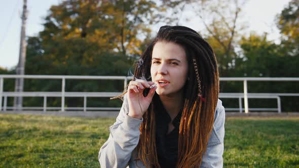 Portrait of Young Pretty Woman with Dreadlocks Smoking Marijuana Joint in Park