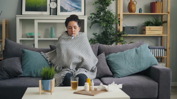 Sick Young Lady Checking Temperature with Thermometer in Mouth in Apartment