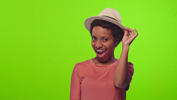 Young Black Woman in Peach T-shirt and Straw Hat Winking at Camera on Chroma Key