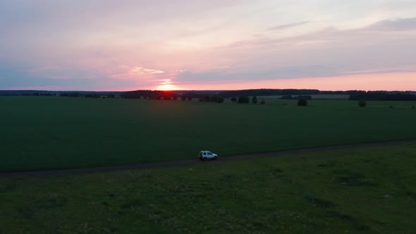 Aerial View of a Car Driving in Nature on a Field at Sunset