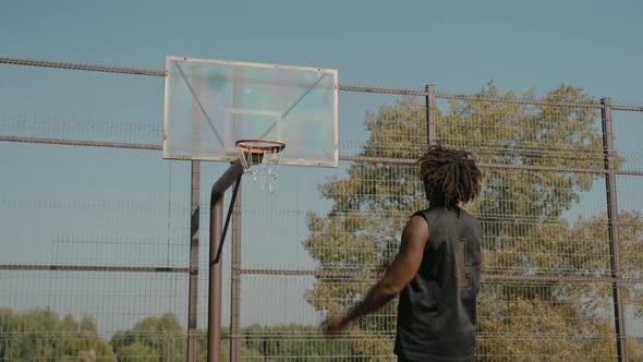 Man Trains Throwing Basketball Ball in Basket on a Street Court on a Sunny Day