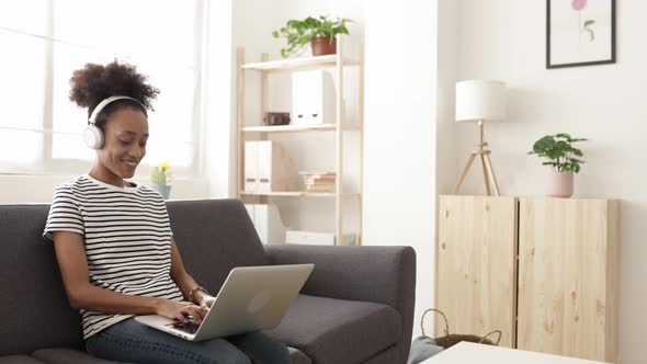 Millennial African Young Woman Listening Music While Using Laptop at Home