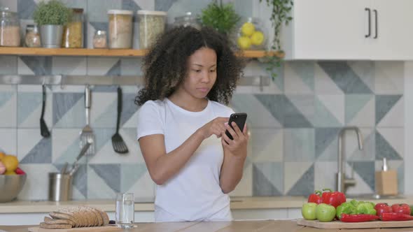 Young African Woman Using Smartphone in Kitchen