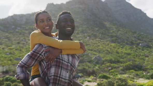 African american man giving piggyback ride to his wife while trekking in the mountains