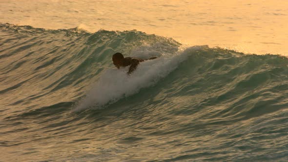 Surfer paddles into wave in late afternoon light, slow motion