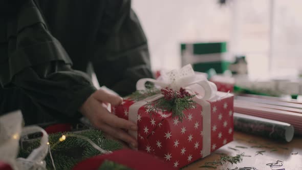 A Young Woman Decorating a Gift on a Wooden Table with Garlands Turns Over and Puts on the Table a