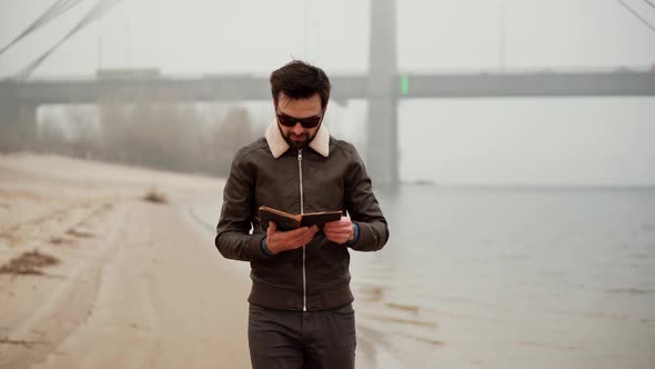 Businessman Relaxing And Enjoying Near River Resting Holding Book. Man Walking On Beach.