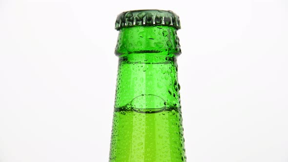 Green glass bottle of beer frosty with water drops rotating over white