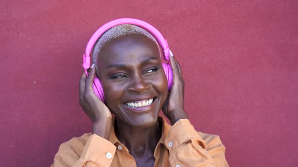 Happy senior Afro woman having fun listening music with wireless headphones