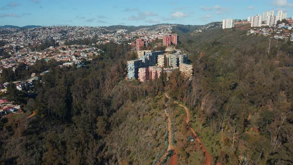 Aerial dolly in of colorful buildings in Quinta Vergara Park surrounded by autumnal forest, Viña del