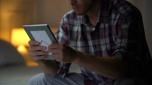 Lonely Man Sitting on Bed Holding Photo Than Rubbing Hair in Despair, Depression