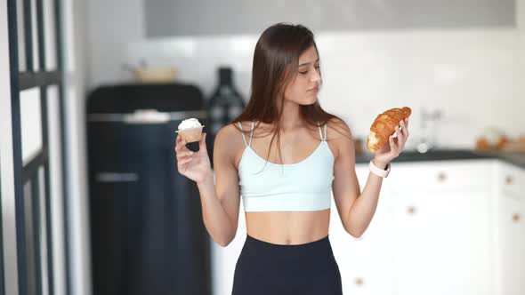 A Young Woman Holds a Croissant and a Cake in Her Hands