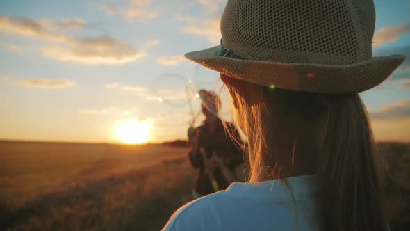 Young Mother and Two Children in the Sunset Catches Soap Bubbles in Meadow. Relax with Children in