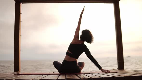 Woman Practicing Yoga and Stretching Spine and Hands Sitting on Mat on Sea Pier Tilting on Sides