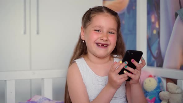 Girl holding smartphone looking at camera smiling. Portrait of cute cheerful young child person