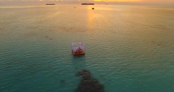 Aerial drone view of a man and woman having dinner on a floating raft boat at sunset