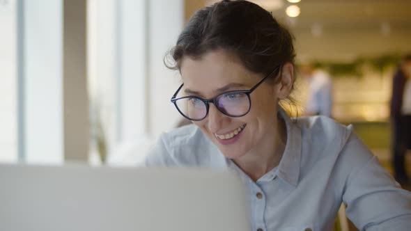 Beautiful Young Female Entrepreneur Sitting at Cafe Table and Having Video Call with Business Team