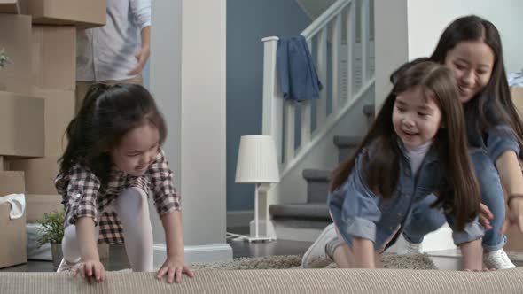 Mother and Daughters Unrolling Carpet in New House