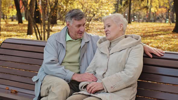 Serene Caucasian Older Married Couple Rest Sitting on Bench in Autumn Park Enjoy Pleasant