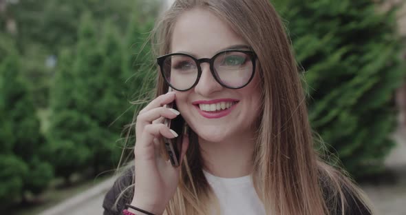 Portrait of Happy Young Girl in Glasses Speaking on a Phone with Smile on Face