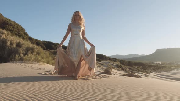 Woman In Gold Dress Walking On Sand Towards Camera