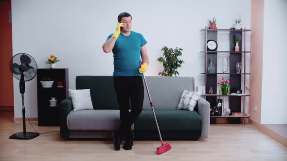 A male cleaner stands with his elbows on the brush talking on the phone