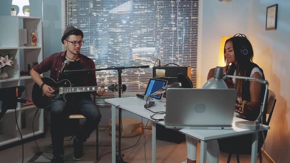 Two Mixed-race Musicians Rehearsing in Home Recording Studio in the Evening