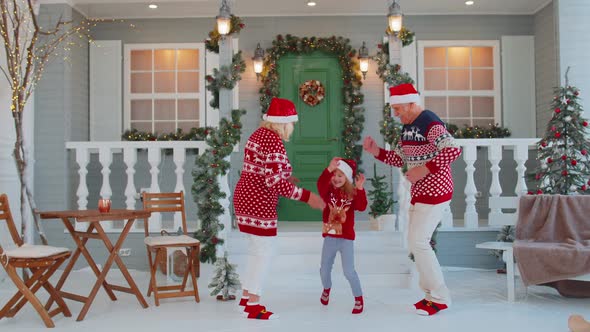 Happy Senior Old Couple Grandparents with Granddaughter Celebrating Dancing Near Christmas House