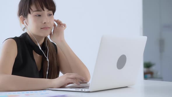 Young asian woman smiling sitting using laptop computer listening music with earphone for relax.