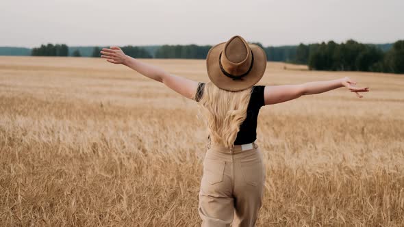 Beautiful Young Blonde Girl in Hat Walking in Wheat Field on Sunset