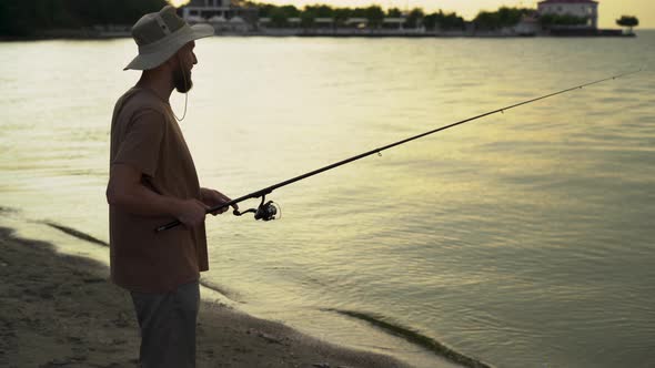 Bearded Man Fisherman at Dawn on the Lake Catches Fish with a Bait