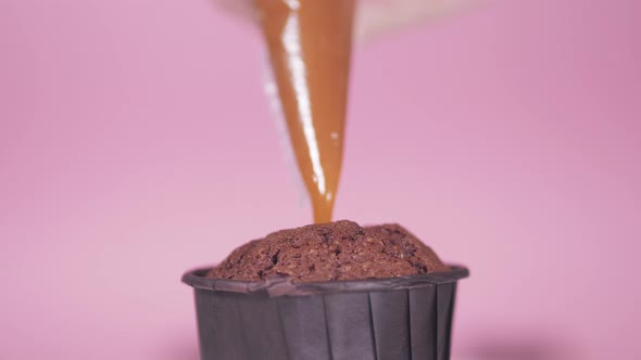 Closeup of Filling a Chocolate Cupcake with Caramel Cream on a Pink Background