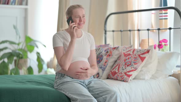 Pregnant Woman Talking on Phone While Sitting on Bed