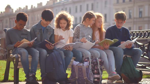 Multiethnic Pupils in Casual Wear Sitting on Street Bench and Reading Books After Classes