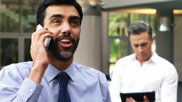 Executive talking on mobile phone his colleague using digital tablet