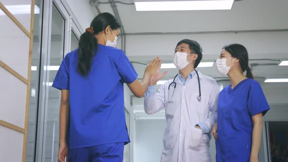 Happy Young Asian Team of Doctor and Nurse in Uniform with Stethoscope and Mask Giving High Five